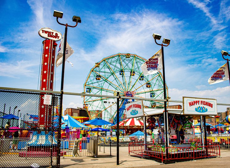 Under a vibrant blue sky, the colorful chaos of Coney Island's amusement park bursts into life