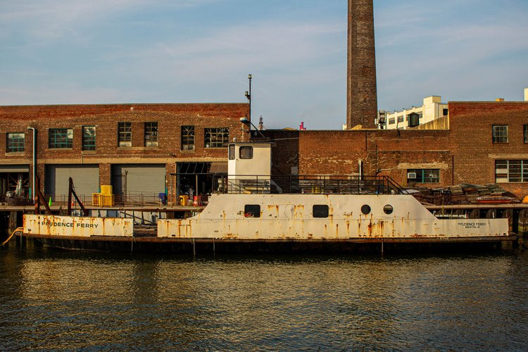 The weathered ferry, moored against a backdrop of industrial brick buildings, tells a story of time...