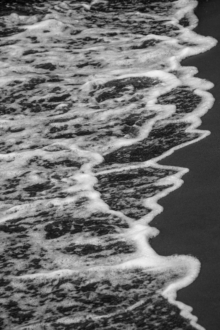 In this striking black-and-white photograph, the ocean's gentle waves caress the shoreline,...