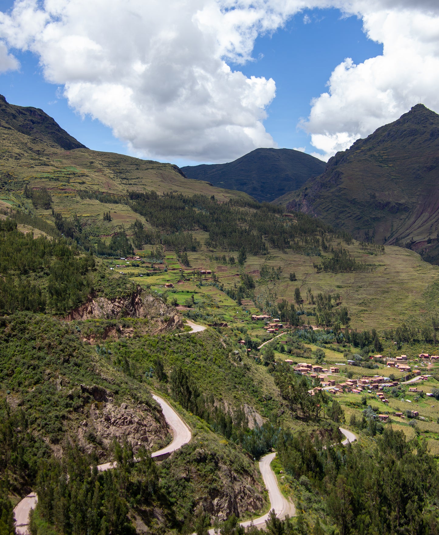 The winding roads carve through the lush, verdant landscape of the Andes, leading the eye towards a...