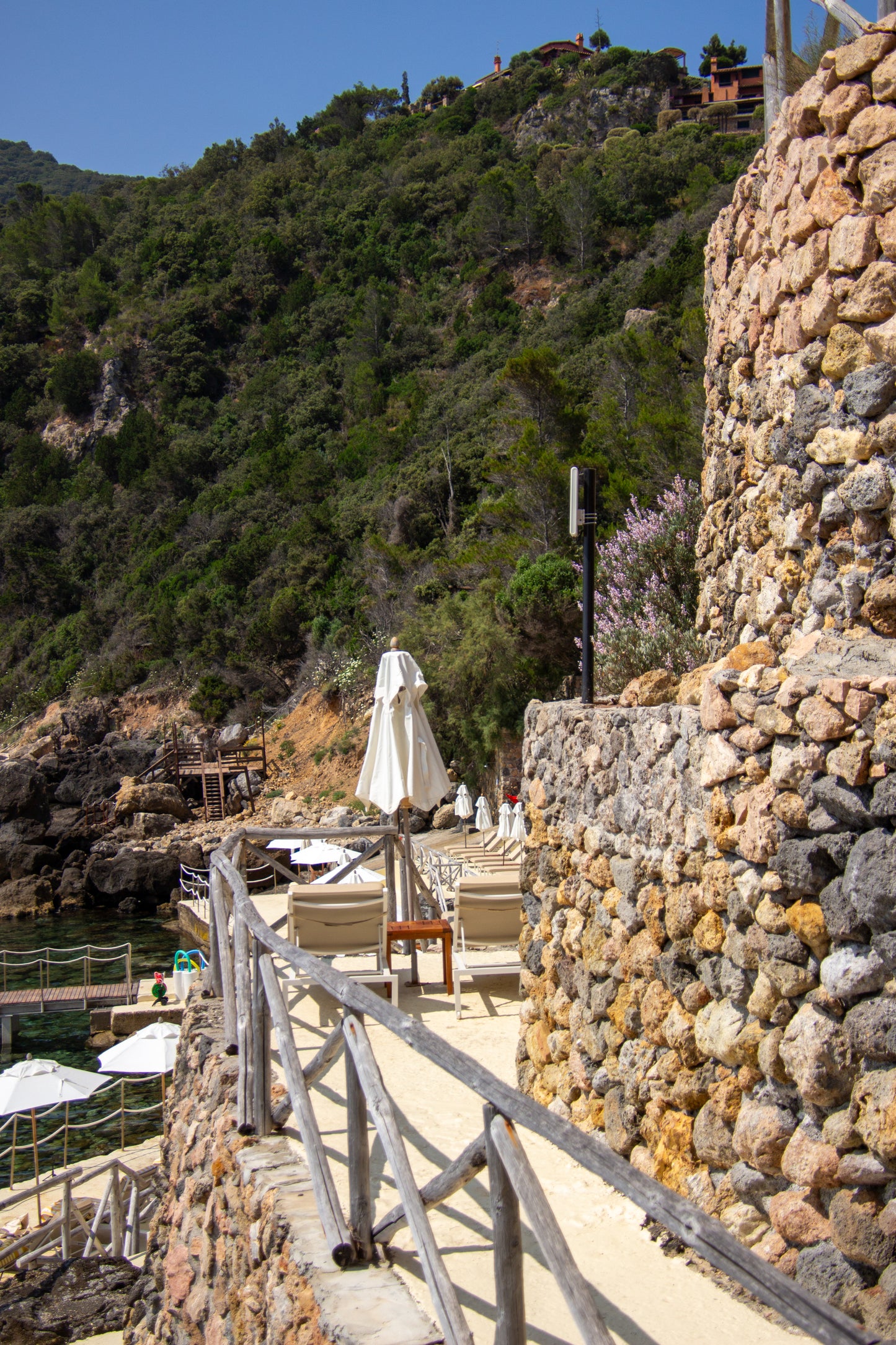 The image captures a serene coastal walkway in Tuscany, with rustic stone walls leading the eye...