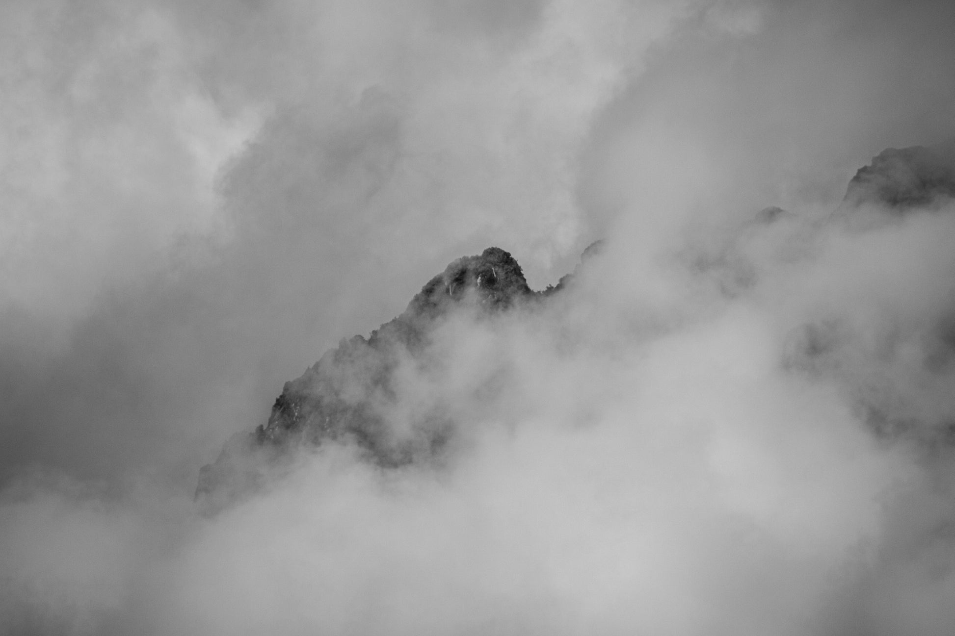 A solitary peak emerges through the swirling clouds, shrouded in mystery and grandeur