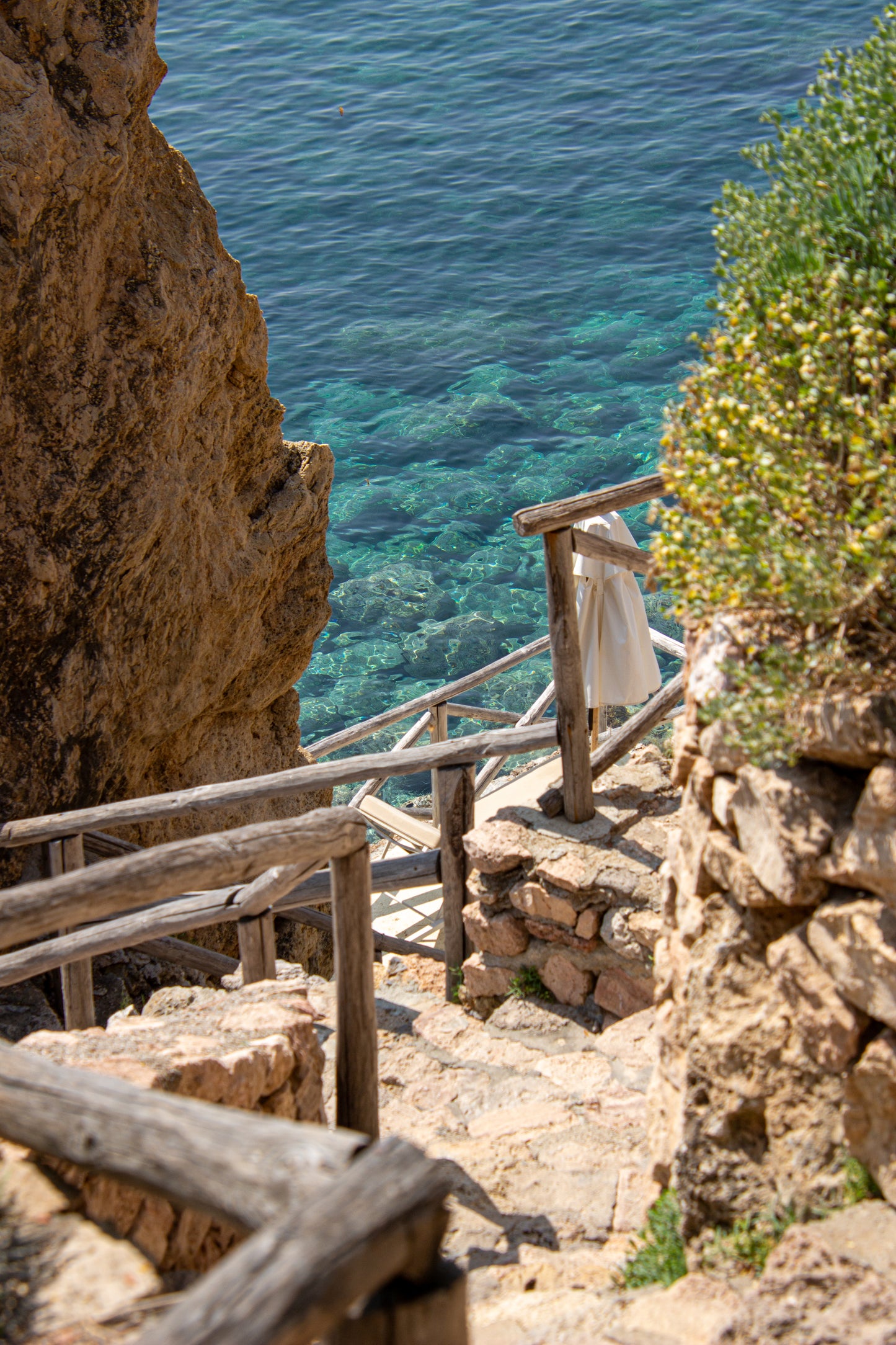 A rustic wooden staircase descends towards the crystalline waters of the Italian coast, framed by...
