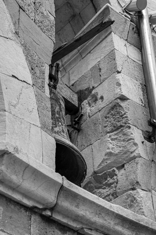 The photograph captures an ancient bell nestled within the rugged stone of an Italian church tower