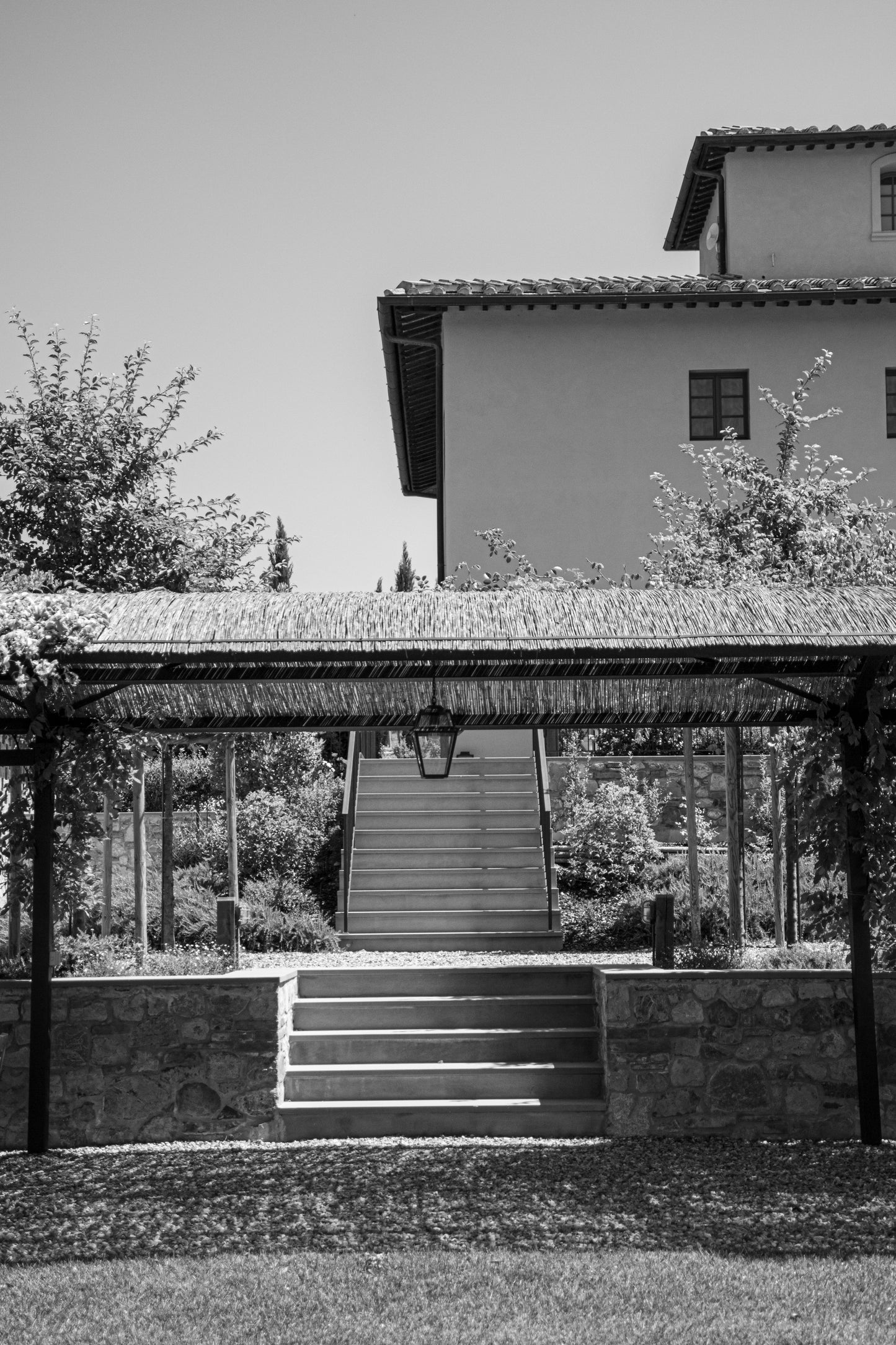 In this serene black-and-white composition, a rustic Italian villa stands quietly beneath a...