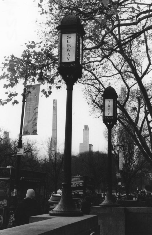 In this evocative black-and-white photograph, the towering presence of two subway lamps stands...